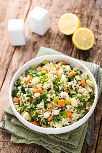 Fresh cooked brown rice with steamed vegetables (broccoli, cauliflower, swiss chard, carrot, celery) in bowl, salt and pepper shaker and lemon in the back (Selective Focus one third into the image)