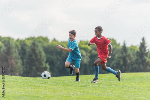 excited multicultural kids playing football on grass