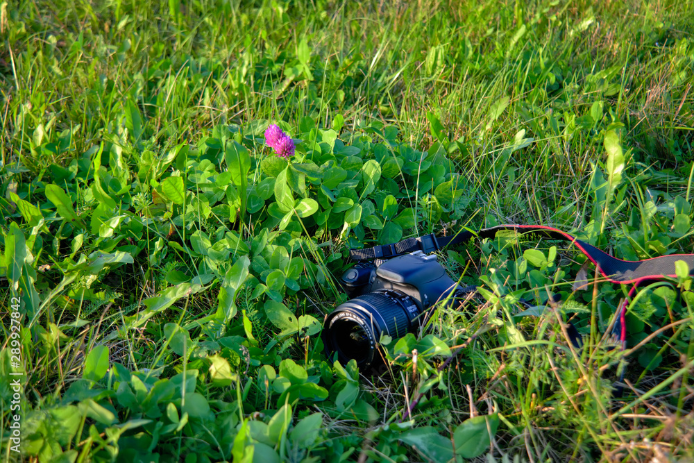 A black digital SLR camera lies on the grass close-up. A black digital SLR camera lies on the grass close-up.