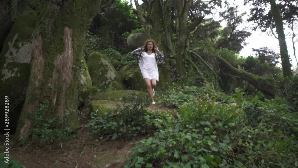 Happy young woman traveler walking in wonderland magic forest, exploring nature. She is in white dress, straw hat and plaid shirt. Happy young woman traveler walking in wonderland magic forest, exploring nature. She is in white dress, straw hat and plaid shirt.