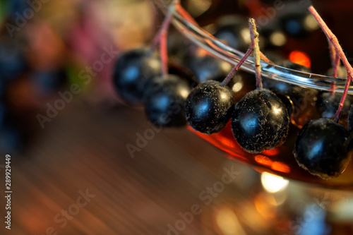 Aronia berries on a glass with homemade wine or tincture. Presentation of the autumn harvest at the farmer's fair. Bokeh and shallow depth of field. Macro photo