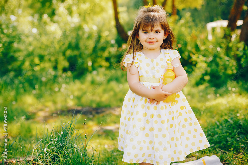 a little girl with beautiful long hair and in a yellow dress is playing in the summer sunshine and sitting on the grass a little girl with beautiful long hair and in a yellow dress is playing in the summer sunshine and sitting on the grass