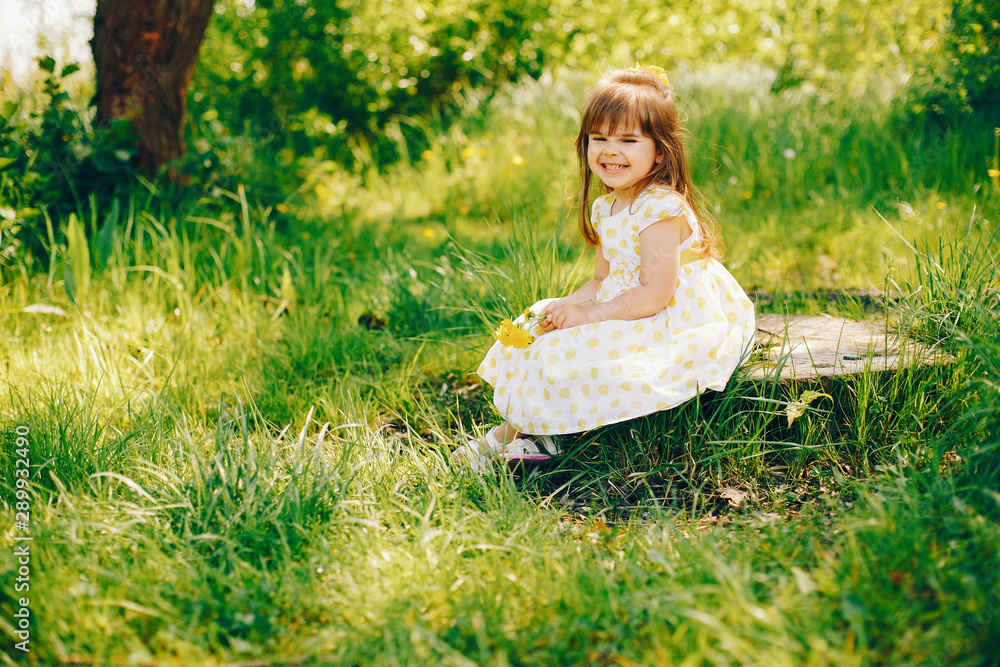 a little girl with beautiful long hair and in a yellow dress is playing in the summer sunshine and sitting on the grass a little girl with beautiful long hair and in a yellow dress is playing in the summer sunshine and sitting on the grass