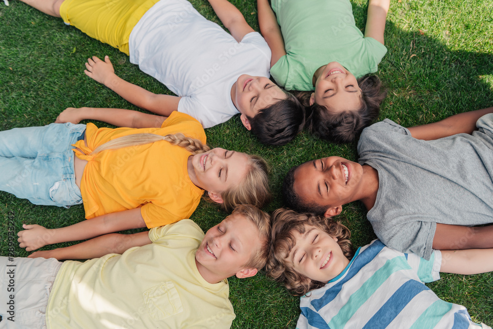 overhead view of happy multicultural kids with closed eyes lying on grass overhead view of happy multicultural kids with closed eyes lying on grass