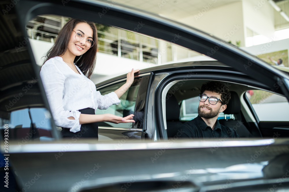 Sales manager woman describing car to customer in showroom Sales manager woman describing car to customer in showroom