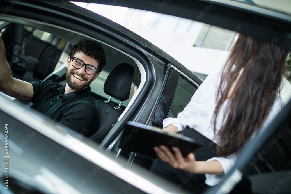 Young woman Manager showing something on a clipboard to the customer in car showroom Young woman Manager showing something on a clipboard to the customer in car showroom