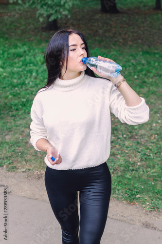 beautiful girl drinks water from a bottle standing in a park