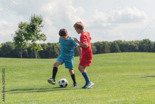 cute friends in sportswear playing football on green grass