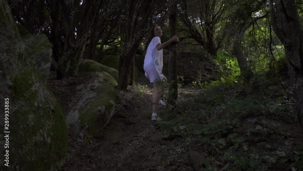 Lady traveler walking in wonderland magic forest. She is in white dress, straw hat and plaid shirt. Forest with huge stones, tall green trees, lianas. Lady traveler walking in wonderland magic forest. She is in white dress, straw hat and plaid shirt. Forest with huge stones, tall green trees, lianas.