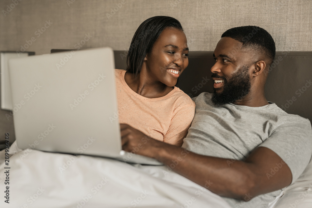 Fototapeta premium Smiling African American couple using a digital tablet in bed