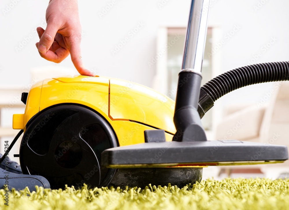 Fototapeta premium Man cleaning the floor carpet with a vacuum cleaner close up