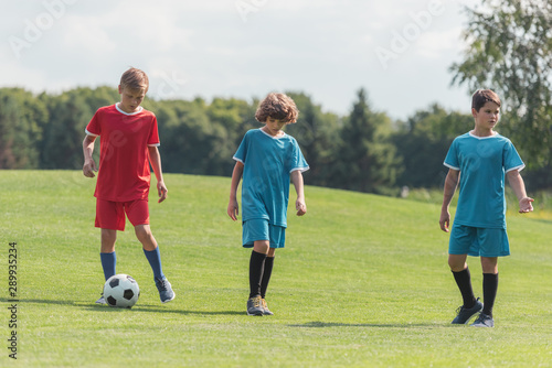 curly boy playing football with friends on green grass
