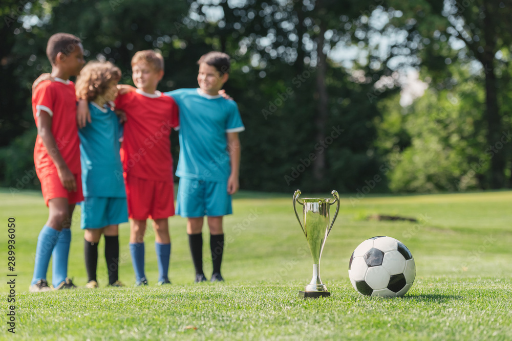 selective focus of trophy and football near cute multicultural winners hugging outside selective focus of trophy and football near cute multicultural winners hugging outside