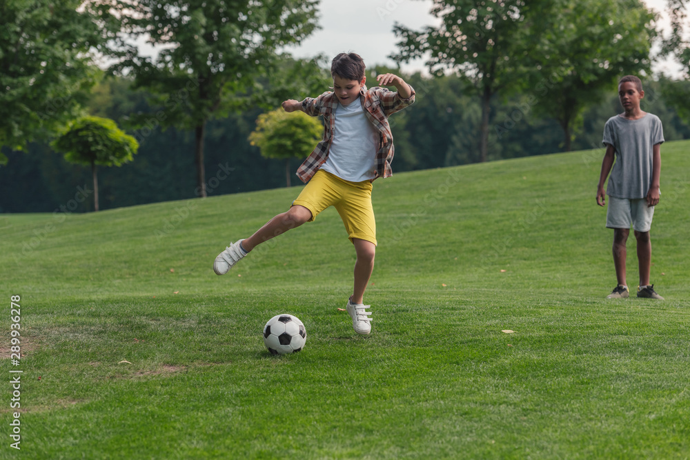 cute african american boy standing on grass near friend playing football cute african american boy standing on grass near friend playing football