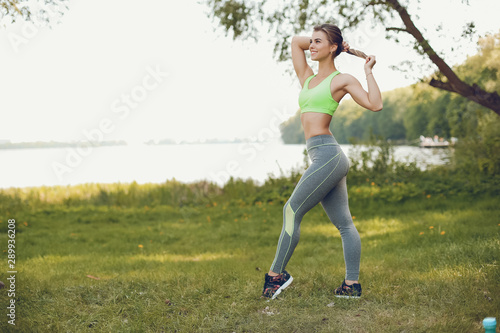 Cute girl standing in a summer forest. Lady have fun in a park. Sports woman in a sportsuit. © hetmanstock2