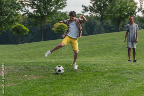 cute african american boy standing on grass near friend playing football