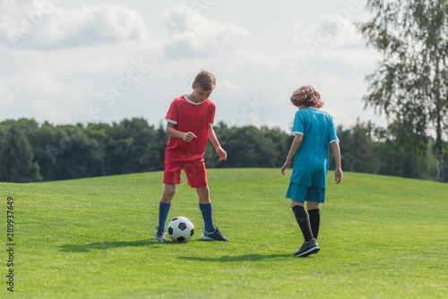 cute curly boy playing football with friend on grass
