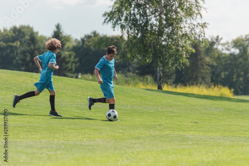 friends in blue sportswear playing football on green grass
