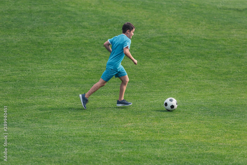 kid in sportswear running on green grass with football