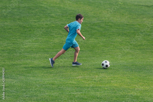 kid in sportswear running on green grass with football