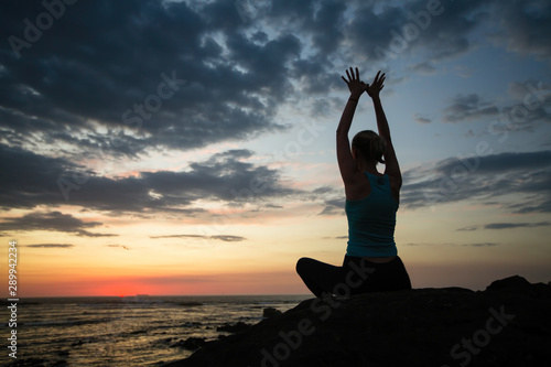 Silhouette of woman yoga on the shore of ocean at evening.