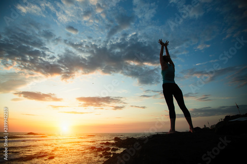 Young woman doing yoga exercises on the seashore during dawn.