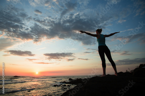 Fototapeta Naklejka Na Ścianę i Meble -  Young fitness woman practicing yoga on the ocean coast during a amazing sunset.