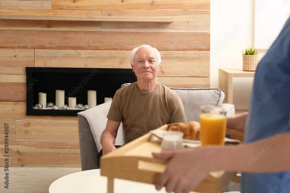 Nurse serving breakfast to elderly man indoors. Assisting senior people Nurse serving breakfast to elderly man indoors. Assisting senior people