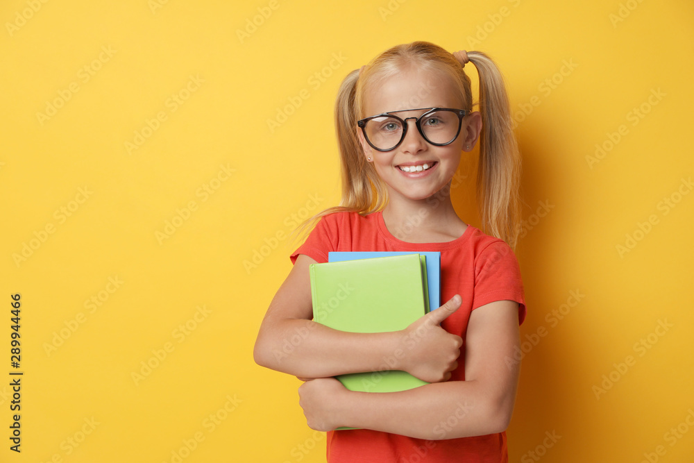 Cute little girl with glasses and books on yellow background. Reading concept Cute little girl with glasses and books on yellow background. Reading concept