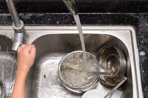 boy washing dishware in the kitchen sink with soapy sponge