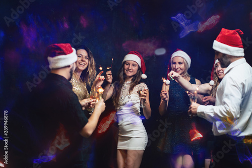 New Year party in night club, Christmas celebration atmosphere. Friends dancing with champagne glasses and sparkles, modern youth life