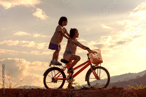 Silhouette two children playing riding bike on mountain at sunset sky background