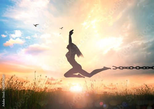 International day for the remembrance of the slave trade and its abolition concept: Silhouette of a girl jumping and broken chains at autumn sunset meadow with her hands raised photo
