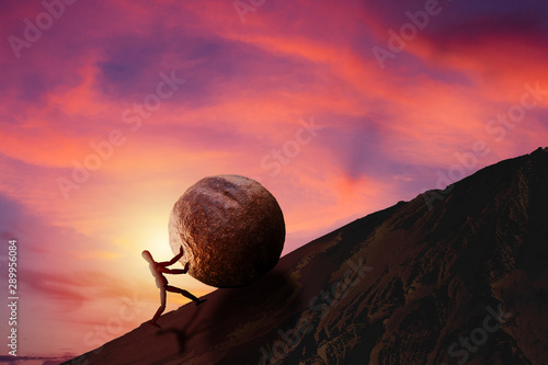 Bilde på lerret Business Challenge and Success Concept : Wooden figure pushing large stone uphill to top of mountain with sunset and beautiful sky in background