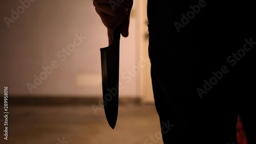 A scary slasher killer holding a terrifying kitchen knife weapon in silhouette before attacking his murder victim. photo