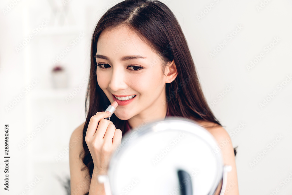 Smiling beautiful woman fresh healthy skin looking on mirror and enjoying applying lips with red lipstick at home.facial beauty and cosmetic concept Smiling beautiful woman fresh healthy skin looking on mirror and enjoying applying lips with red lipstick at home.facial beauty and cosmetic concept