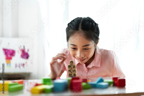 Little cute girl enjoy while playing wooden blocks toys on table at home