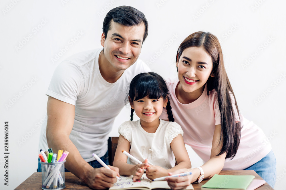 Happy family father and mother with daughter learning and writing in notebook with pencil making homework at home.Education concept Happy family father and mother with daughter learning and writing in notebook with pencil making homework at home.Education concept