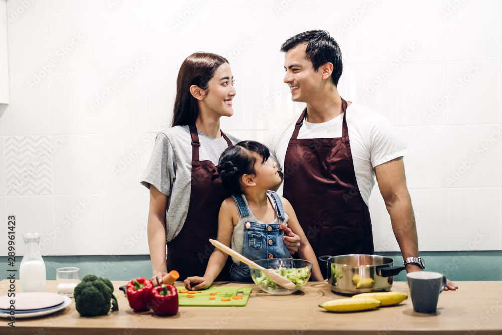 Happy family father and mother with daughter cooking and preparing meal together in the kitchen