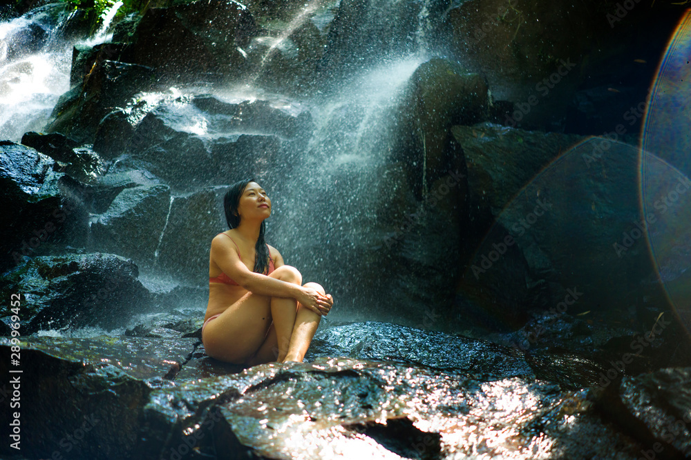 Fototapeta premium natural portrait of young beautiful and happy Asian Chinese woman in bikini enjoying nature at tropical paradise waterfall with magical feeling in soul inspiration