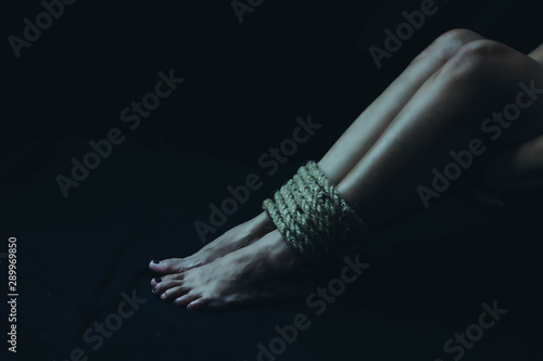 Close up of woman's legs bondage with old rope in the dark room, Conceptual image sex abuse and Slave trade prevention concept with copy space.