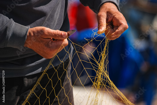 Close up detail of Fisherman hands repairing net with knife.