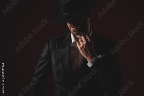 mysterious young man fixing collar on black background