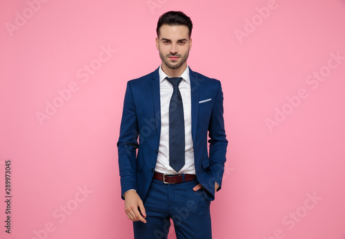 attractive young man wearing navy blue suit on pink background