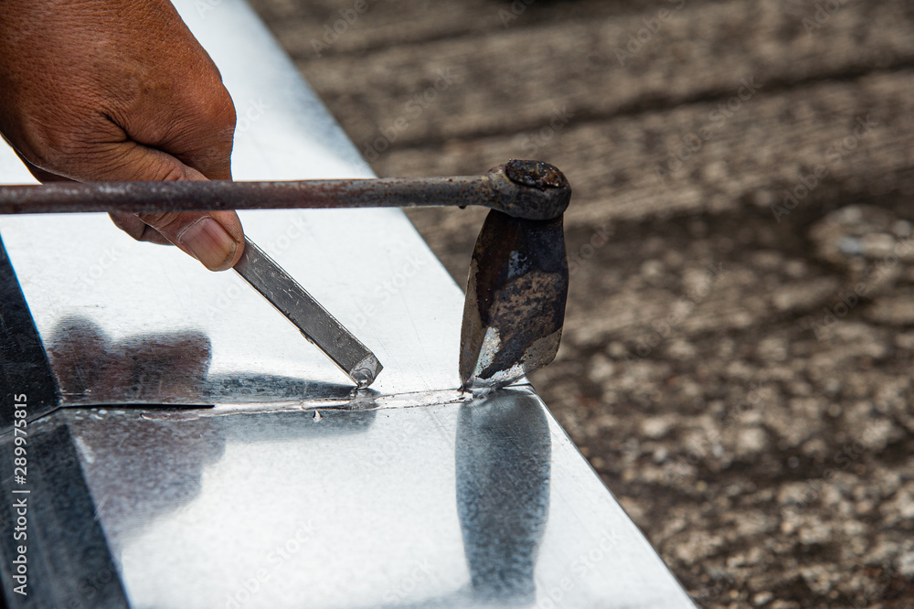 Closeup hand using old fashioned bonding to solder aluminium gutter roof. Stock Photo Adobe Stock