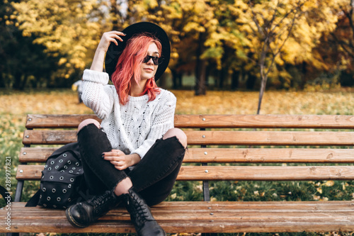 Pretty girl with red hair and hat relaxing on the bench in the park, autumn time.