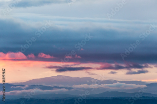 View of colorful clouds at sunset, over and below a mountain