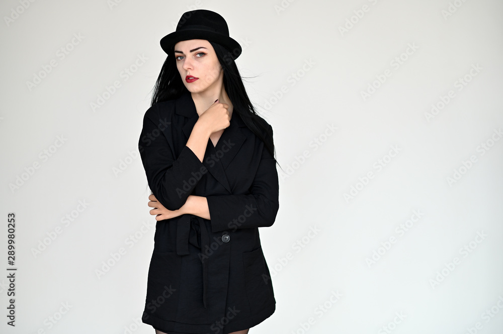 Concept portrait of a pretty brunette girl with long black hair in a hat and a business suit on a white background in studio. Standing right in front of the camera in various poses. Concept portrait of a pretty brunette girl with long black hair in a hat and a business suit on a white background in studio. Standing right in front of the camera in various poses.