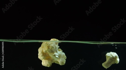 An appetizing slice of cauliflower beautifully falls into the water with bubbles and splashes on a black background, slow motion, closeup photo