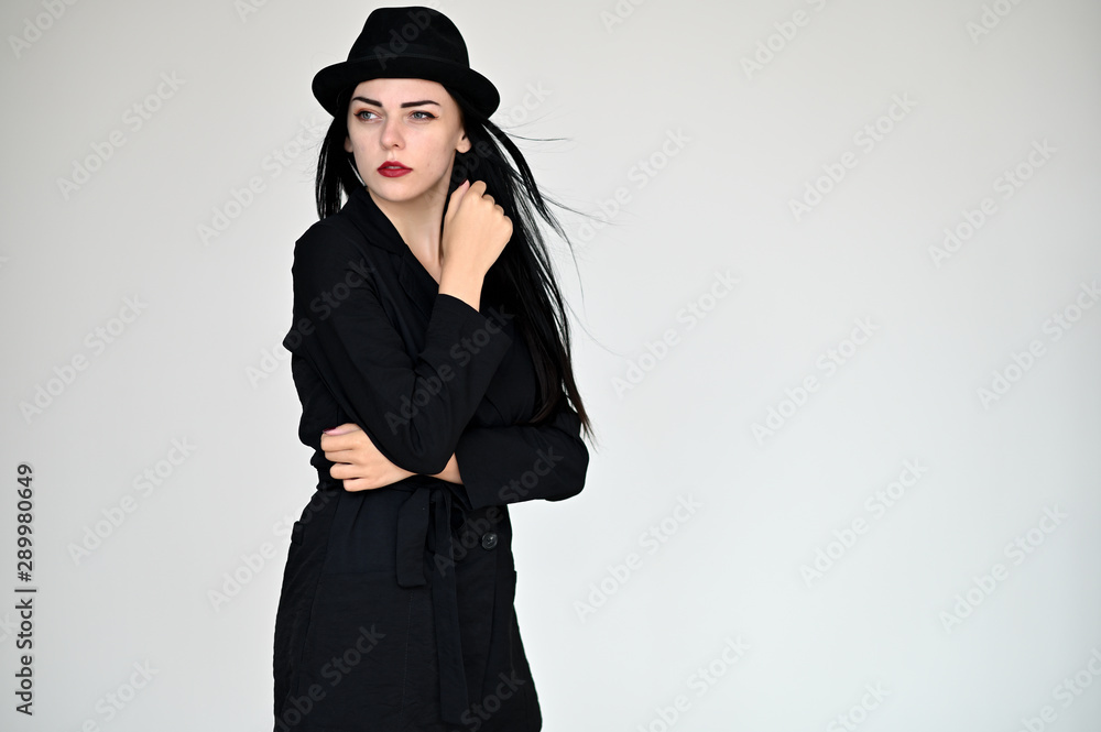 Concept portrait of a pretty brunette girl with long black hair in a hat and a business suit on a white background in studio. Standing right in front of the camera in various poses. Concept portrait of a pretty brunette girl with long black hair in a hat and a business suit on a white background in studio. Standing right in front of the camera in various poses.